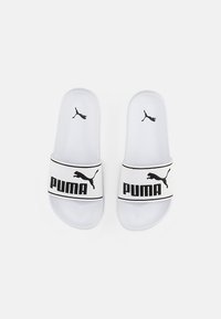 Biele sklzlepky Puma s textúrovaným pásikom, ktorý má čierne logo a akcenty. Ploché podrážky s hladkým povrchom. Odolný materiál.
