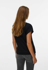 T-shirt noir à manches courtes avec des ourlets roulés, en coton doux, associé à un jeans gris délavé, vu de dos. Texture lisse.