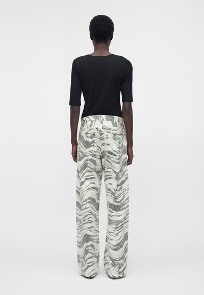 Άτομο που στέκεται με την πλάτη, φοράει μαύρο τοπ με μισά μανίκια και παντελόνια ψηλόμεσα, φαρδιά με γκρι και λευκό σχέδιο ζέβρας.