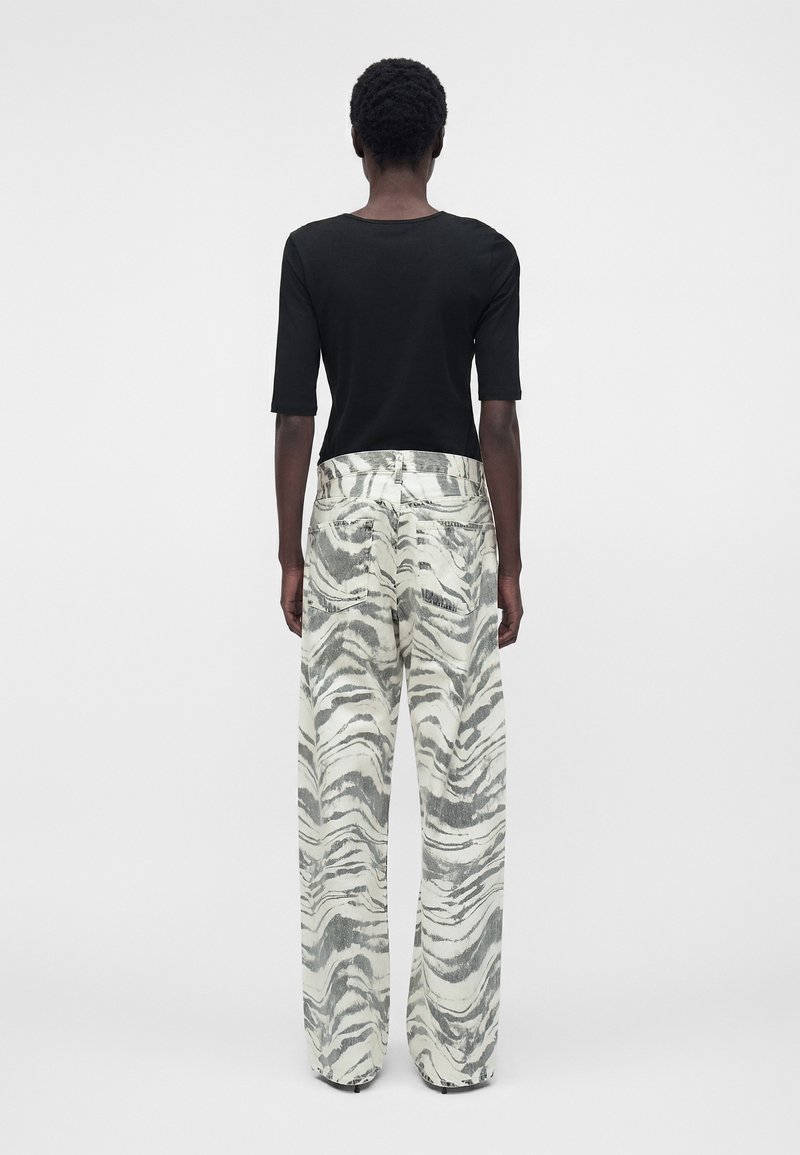 Person steht mit dem Rücken zum Betrachter, trägt ein schwarzes Halbarmoberteil und hoch taillierte, weit geschnittene Hosen mit einem grauen und weißen Zebramuster.