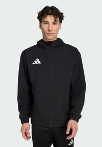 Μαύρο ελαφρύ μπουφάν με κουκούλα, με κλείσιμο φερμουάρ και ελαστικούς καρπούς. Διαθέτει λευκό τριγωνικό λογότ υπο στο πάνω αριστερό μέρος του στήθους.