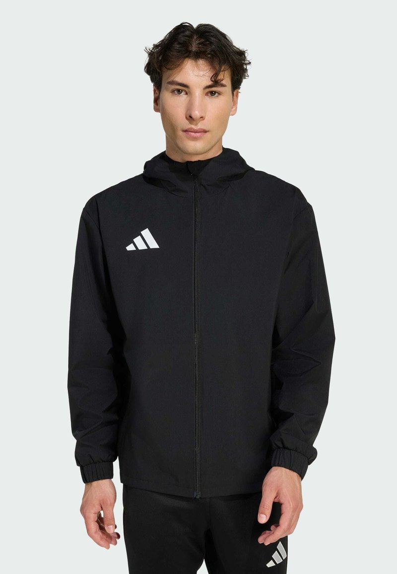 Μαύρο ελαφρύ μπουφάν με κουκούλα, με κλείσιμο φερμουάρ και ελαστικούς καρπούς. Διαθέτει λευκό τριγωνικό λογότυπο στο πάνω αριστερό μέρος του στήθους.