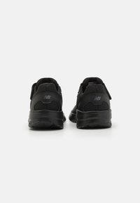 Black athletic shoes with a mesh and synthetic upper, padded collar, and flexible sole. Features adjustable straps and logo accents on heels.
