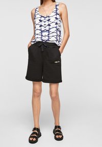 Vit linne med blått tie-dye-mönster, svarta shorts med dragsko och två fickor, samt svarta sandaler med tjock sula.