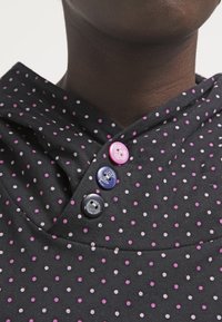 Tela negra con pequeños lunares rosas y morados, que cuenta con una capucha y tres botones decorativos en rosa, marino y negro.