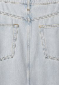 Lys blå denimstoff har et enkelt bakdesign med to lommer, synlig søm i en kontrasterende gul farge. Glatt tekstur med subtile falmede områder.