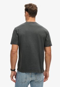 Donkergrijze shirt met korte mouwen en een ronde halslijn, zachte textuur en zichtbare stiksels. Draag het met lichtblauwe denim jeans.