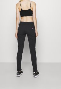 Zwarte elastische joggers met een slanke pasvorm en twee achterzakken, voorzien van een klein logo. Gecombineerd met een zwarte cropped top en sneakers.