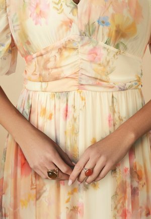 Lillelille lillede kleit pastelltoones, lühikeste ja puhvidega varrukatega. Rikkalikult volangidega bodice ja voogav seelik. Käed ehtitud kuldsete sõrmustega, üks pruuni kalliskiviga.