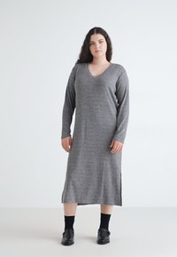 Rochie gri cu maneci lungi, cu dungi, cu un decolteu în V și laterale fâșiate, realizată dintr-un material tricotat. Poartă șosete și pantofi negri.