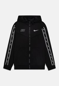 Svart zip-up hoodie med huva, med vita Nike-logotyper på bröstet och ärmarna, samt vita detaljer längs sidorna. Mjuk tyg.