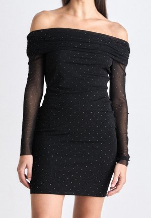 Mujer con un vestido negro ajustado sin hombros, mangas largas transparentes y pequeños lunares blancos por todo el vestido.