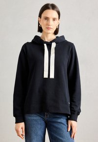 Tamsiai mėlynas džemperis su švelnaus audinio, su raišteliu ant kaklo kreminės spalvos, turintis sutraukiamus rankogalius ir apykaklę, bei paprastą logotipo detalę apačioje.