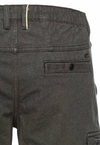 Dunkelgraue Jeans mit einer geknöpften Gesäßtasche, strukturiertem Stoff und sichtbaren Steppnähten entlang des Bundes.