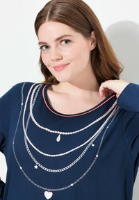 Mörkblå topp med rund halsringning och ljus korallfärgade detaljer, med silverkedjor och charm-mönster, inklusive hjärtan och droppar.