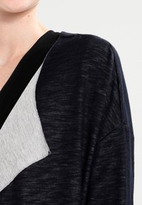 Top nero e grigio con scollo a V, design asimmetrico, texture morbida e vestibilità ampia con pannello di colore contrastante.