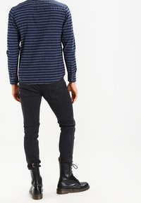 Camicia a maniche lunghe blu navy con strisce bianche, abbinata a jeans neri slim-fit e stivali neri stringati con suola spessa.