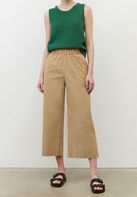 Grön texturerad ärmlös topp, beige vida byxor med elastisk midjeband, och svarta sandaler med en dekorativ spänne.