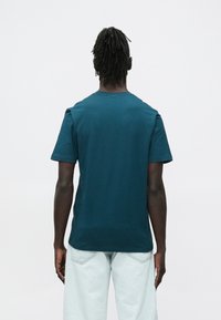 �Μπλουζάκι κοντομάνικο σε τιρκουάζ χρώμα κατασκευασμένο από απαλό ύφασμα, με απλό σχέδιο λαιμού τύπου crew και άνετη εφαρμογή. Φορεμένο με τζιν ανοιχτού χρώματος.