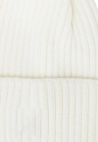 Biała, prążkowana czapka beanie z podwiniętym mankietem. Materiał wydaje się być miękki i elastyczny, z delikatnymi, pionowymi paskami w całej strukturze.