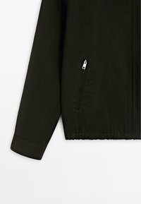 Zwarte jas met mouw en onderlichaam met een zak met rits en elastische tailleband op een witte achtergrond.