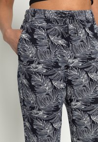 Calças de jogging em azul-marinho com padrão de folhas de palmeira brancas, apresentando uma cintura elástica, fecho com cordão e bolsos laterais. Feitas de tecido suave.