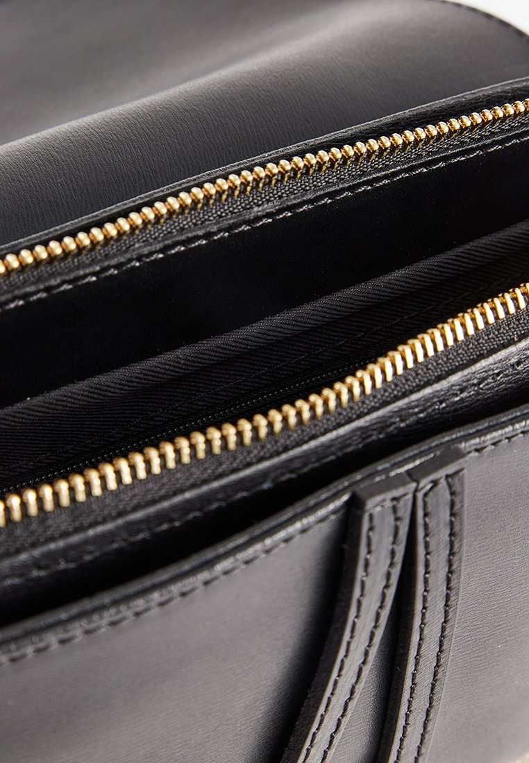 Wn�ętrze czarnej skórzanej torby z złotymi metalowymi zamkami błyskawicznymi. Posiada gładką teksturę i dwie komory, ukazujące staranne szwy.