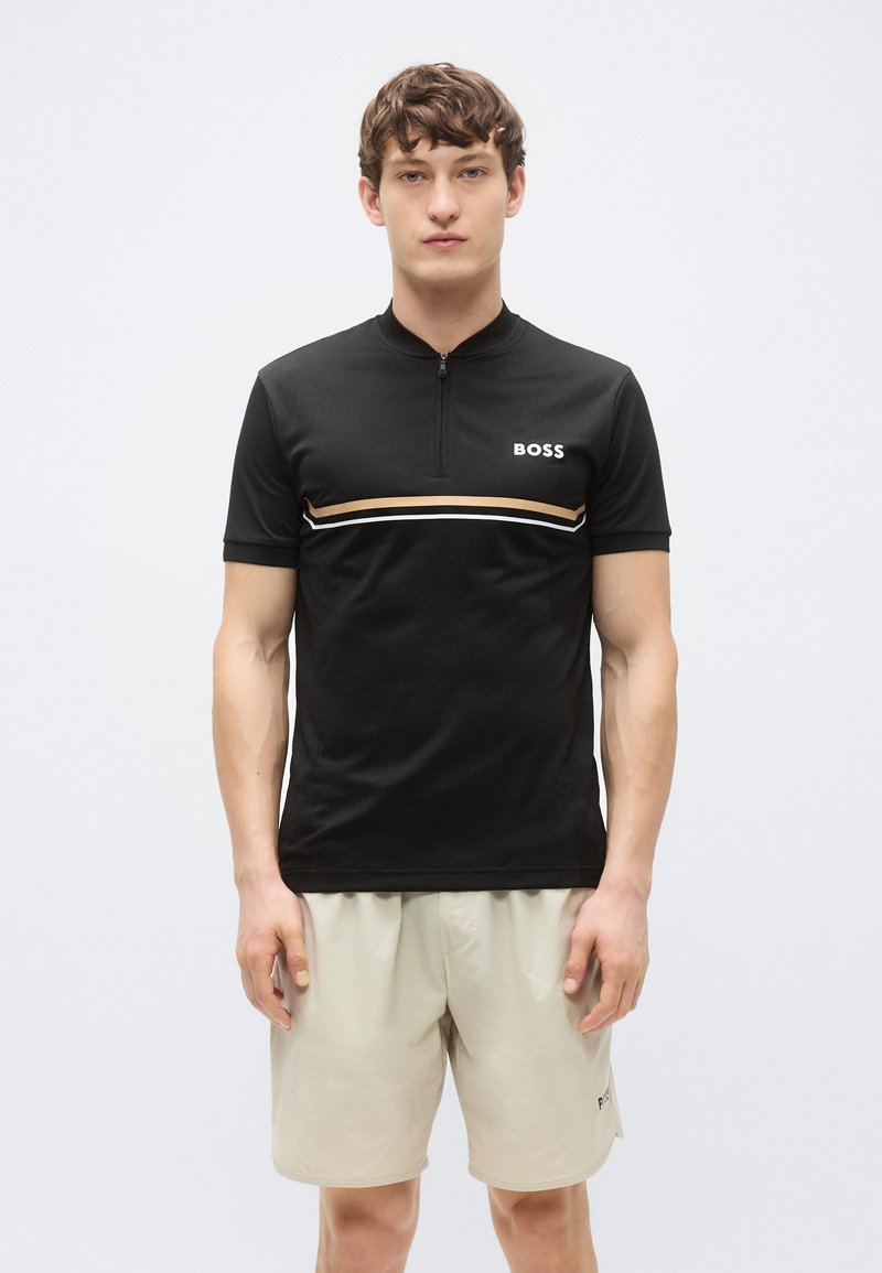 Sort t-skjorte med korte ermer og kvart glidelås, med horisontale beige og hvite striper, "BOSS"-logo på brystet, kombinert med beige shorts.