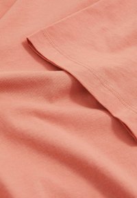 Tricou din bumbac de culoare coral moale, cu o textură fină, având un decolteu rotund și mâneci scurte. Cusături îngrijite pe margini.