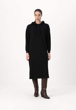 Black hoodie dress with long sleeves, a drawstring hood, and calf-length design. Paired with brown patterned high-heeled boots.