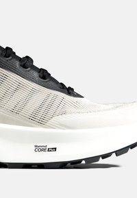 Gros plan d'une chaussure de sport beige et noire avec une tige en mesh respirant et une semelle épaisse blanche portant l'inscription "Mammut CORE Plus".