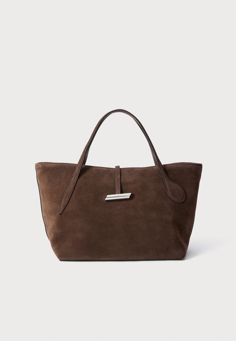 Bolsa tote em camurça castanha com duas alças suaves, uma alça vertical com um detalhe prateado e um topo largo e aberto. Textura suave, design minimalista.