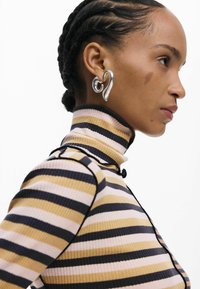 Triibuline kõrge kaelusega kampsun roosakas, kuldse ja mereväe toonides. Omadusi on sooniline tekstuur ja must ääristus. Kandmisega kaasneb hõbedane südamekujuline kõrvarõngas.