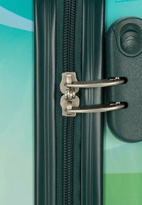 Meccanismo della cerniera verde con accessori in metallo argentato, attaccato a una superficie testurizzata con un gradiente di colore, che mostra nuance di blu e verde.