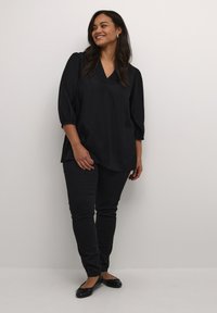 Blusa negra con cuello en V y mangas abullonadas 3/4, combinada con pantalones negros ajustados y bailarinas. Tejido suave con un ajuste relajado.