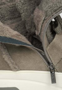 Bruine suède schoen met een gestructureerde stof, een binnenfleece-voering, een grijze rits en een witte rubberen zool. Maatlabel zichtbaar op 39.