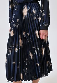 Marineblauer Faltenrock mit beigen und weißen Blumenmustern, aus glattem Stoff. Verfügt über einen taillierten Bund und lange, schwingende Falten.