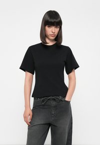 Svart kortermet t-skjorte laget av et glatt, lett stoff med en kroppsnær silhuett og minimalistisk design. Kombinert med mørke grå jeans.