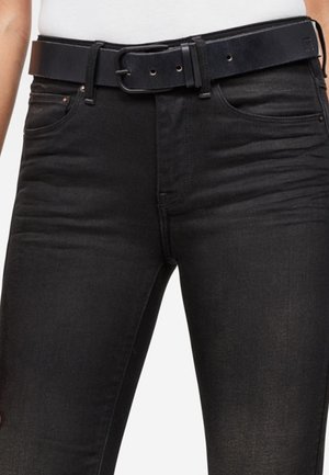 Zbliżenie na czarne dżinsy z przednimi kieszeniami i czarnym paskiem, noszone z białą włożoną koszulą.