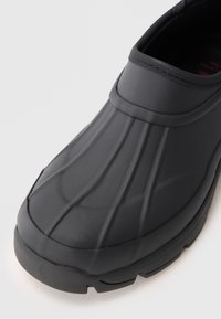 Black rubber shoe with a smooth finish, ridged top, and a sturdy sole. Features a rounded toe and minimalistic design with no visible hardware.