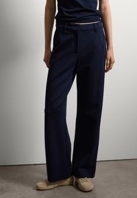 Pantalones de talle alto de color navy con piernas anchas, confeccionados en un tejido suave. Presentan bolsillos frontales y un cierre de un solo botón.