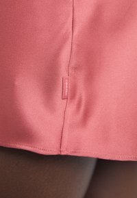 Rosa, glatt stoff med en sømløs hem og en liten Calvin Klein-merkelapp på siden, som viser enkel design og lett tekstur.