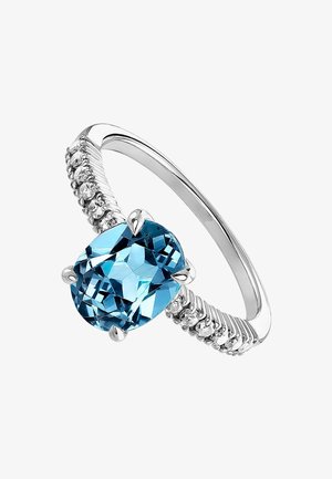 Anillo de plata con una gran piedra gema azul en corte cojín, rodeada de pequeños acentos claros. La banda tiene una textura retorcida.