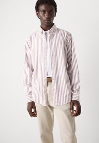Camicia a righe bianca e rosa chiaro, realizzata in cotone. Presenta un colletto, maniche lunghe e una vestibilità rilassata. Indossata sopra una t-shirt bianca.