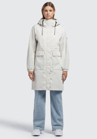Parka leggera, di lunghezza al ginocchio, in tessuto bianco sporco con cappuccio, coulisse regolabili e due tasche anteriori; design pulito e minimale.