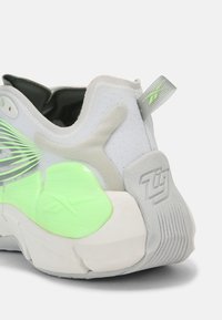 Talonnette de basket blanche et gris clair avec des accents vert néon, un onglet de traction et une semelle texturée montrant les logos de la marque et les détails du design.