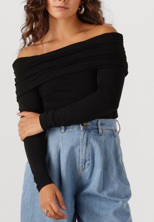 Zwarte off-shoulder top met lange mouwen, gemaakt van zacht materiaal. Gepaard met hoge, lichtblauwe denim broeken met een ontspannen pasvorm.