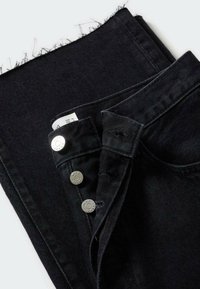 Jean en denim noir avec ourlet effiloché et trois boutons-pression argentés partiellement ouverts sur fond blanc.