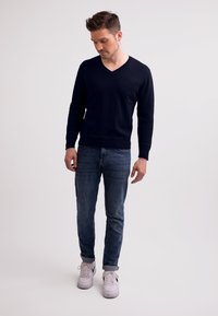 Marinblå V-ringad tröja, figursydd design, ribbade ärmslut, tillsammans med mörka denimjeans och vita sneakers. Slät textur, enkel silhuett.