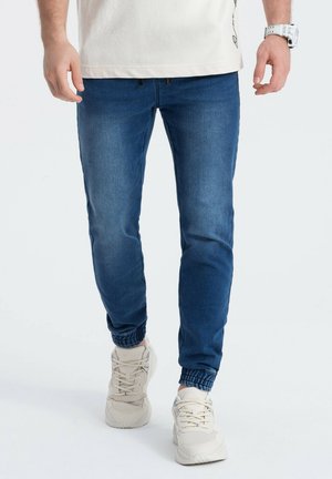 Blauwe denim joggerbroeken met elastische boorden, voorzien van een soepele textuur en een slim-fit silhouet. Gekoppeld aan lichtgekleurde sneakers.